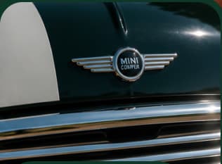L’écusson Mini Cooper ailé sur le capot vert anglais, au-dessus de la calandre chromée.