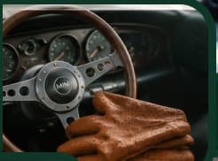 Un volant à trois branches et une paire de gants de conduite en cuir fauve posée dessus.